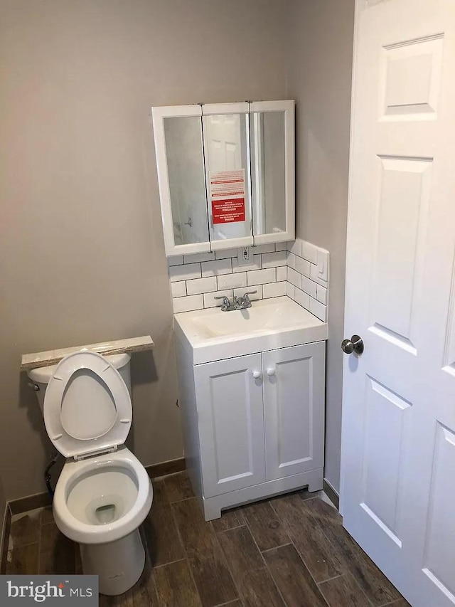bathroom featuring tasteful backsplash, vanity, baseboards, wood finish floors, and toilet