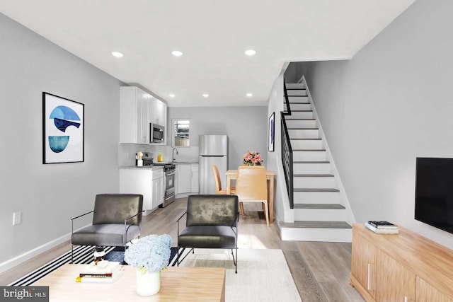 living room featuring baseboards, light wood-style flooring, recessed lighting, and stairs