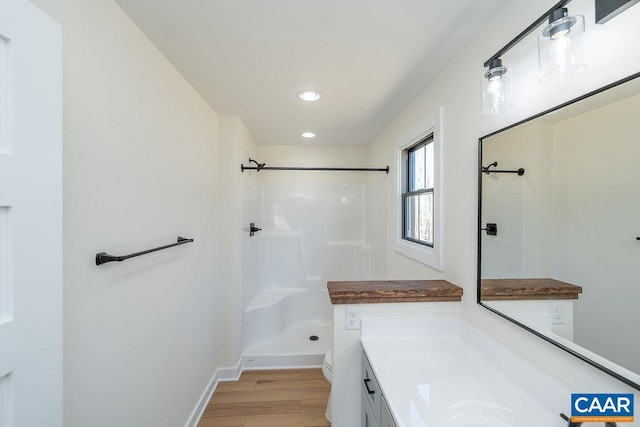 full bathroom with toilet, a shower, vanity, wood finished floors, and baseboards