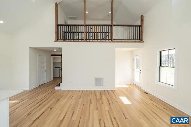 unfurnished living room with baseboards, visible vents, light wood-type flooring, and washer / dryer