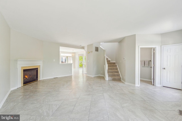 unfurnished living room with an inviting chandelier, visible vents, a glass covered fireplace, baseboards, and stairway