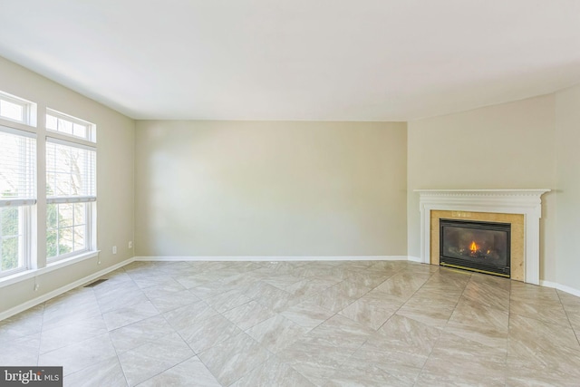 unfurnished living room featuring a glass covered fireplace, baseboards, plenty of natural light, and visible vents
