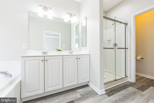 full bathroom featuring a sink, double vanity, wood finished floors, a bath, and a stall shower