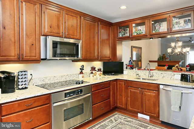 kitchen with glass insert cabinets, a sink, a chandelier, stainless steel appliances, and light stone counters