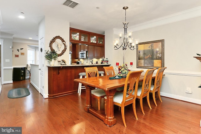 dining area with baseboards, a chandelier, crown molding, visible vents, and wood finished floors