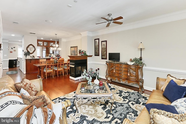 living area featuring baseboards, crown molding, visible vents, ceiling fan with notable chandelier, and wood finished floors