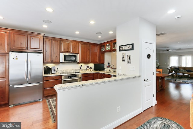 kitchen featuring light stone counters, a peninsula, light wood-style flooring, appliances with stainless steel finishes, and a sink