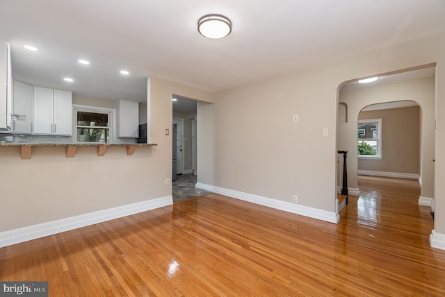 unfurnished living room featuring arched walkways, baseboards, recessed lighting, and light wood-type flooring