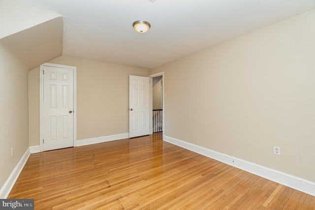 empty room with baseboards, vaulted ceiling, and light wood-style floors
