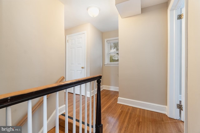 hallway featuring baseboards, an upstairs landing, and wood finished floors