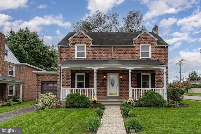 view of front of house featuring a chimney, a front yard, covered porch, and brick siding