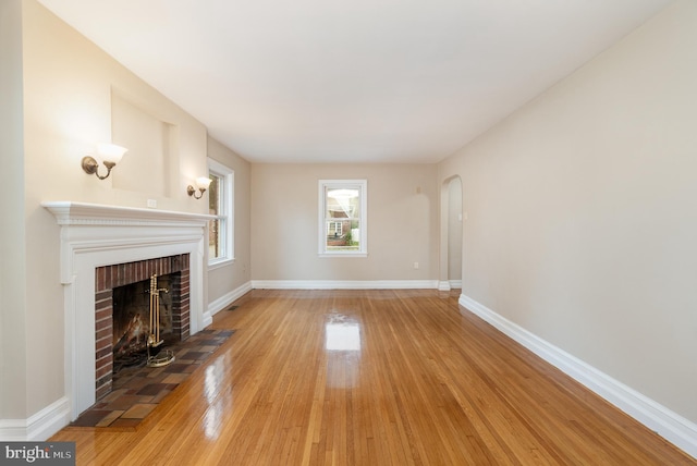 unfurnished living room featuring arched walkways, baseboards, a fireplace, and light wood-type flooring