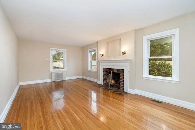 unfurnished living room featuring radiator, baseboards, light wood-style floors, visible vents, and a brick fireplace