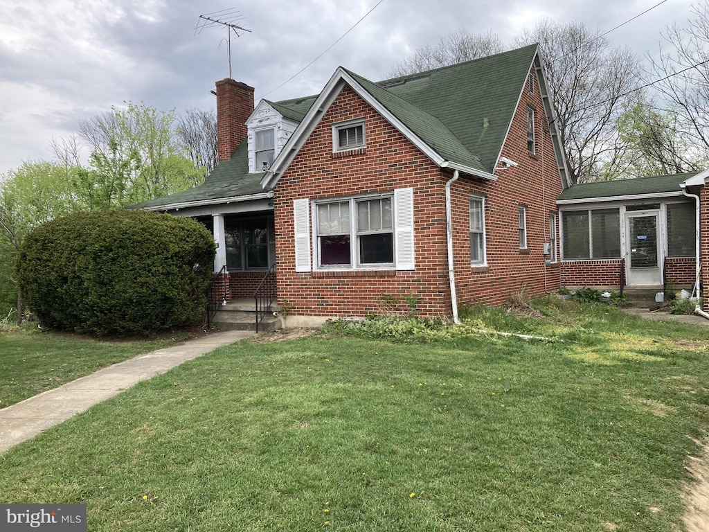 view of front of home featuring brick siding, a chimney, a shingled roof, and a front lawn