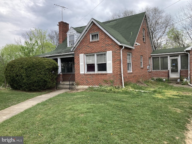 view of front of home featuring brick siding, a chimney, a shingled roof, and a front lawn
