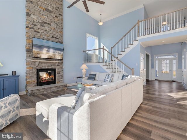 living room featuring baseboards, wood finished floors, a ceiling fan, and a stone fireplace