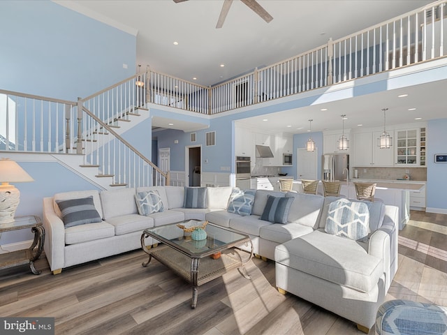 living area featuring stairs, baseboards, a high ceiling, light wood finished floors, and a ceiling fan