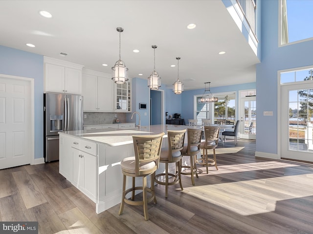 kitchen with light countertops, stainless steel fridge with ice dispenser, a spacious island, glass insert cabinets, and wood finished floors