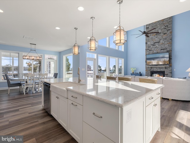 kitchen with a sink, dishwasher, a stone fireplace, dark wood-style floors, and ceiling fan