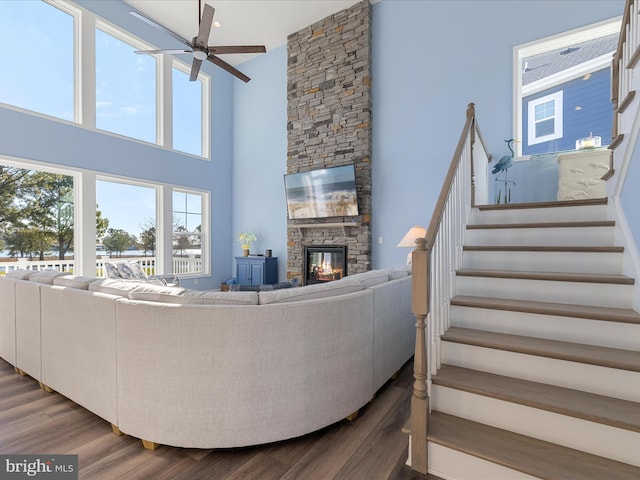 living room with stairs, a ceiling fan, a fireplace, a high ceiling, and wood finished floors