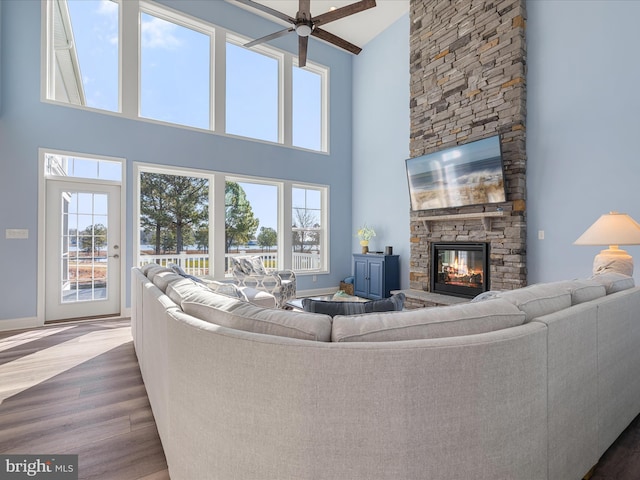 living room featuring baseboards, ceiling fan, wood finished floors, a towering ceiling, and a stone fireplace