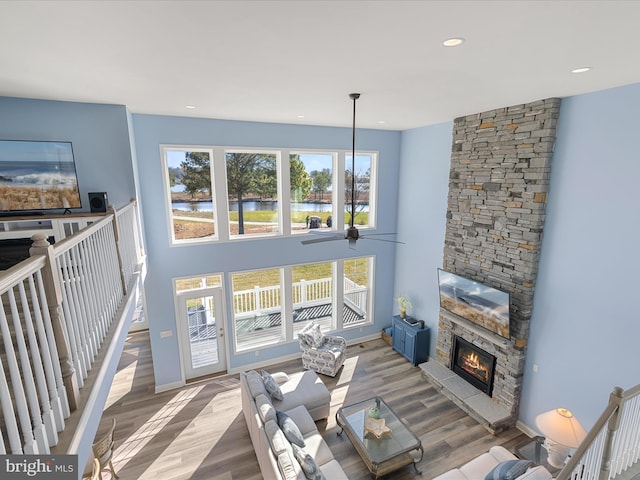 living area featuring baseboards, wood finished floors, a ceiling fan, and a stone fireplace