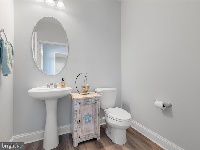 half bath featuring baseboards, toilet, a sink, and wood finished floors