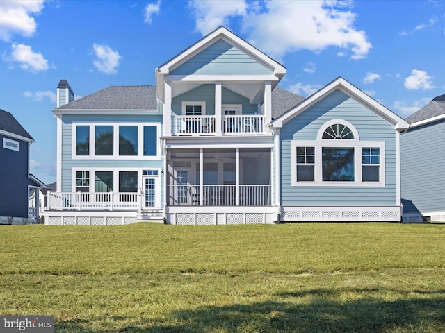 rear view of house with a balcony, a shingled roof, a sunroom, and a lawn