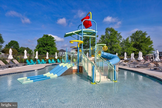 pool featuring fence, a patio, a water slide, playground community, and a water play area