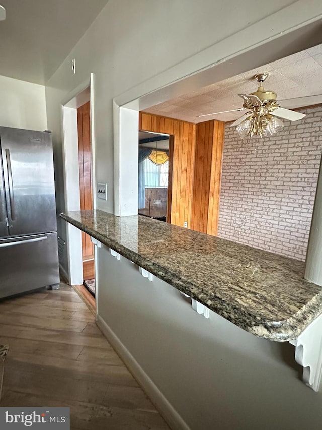 1224 Sheridan Ave, Baltimore, MD 21239 - kitchen featuring dark stone countertops, wood finished floors, brick wall, freestanding refrigerator, and ceiling fan