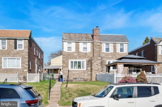 townhome / multi-family property with a gazebo, a chimney, a front lawn, stone siding, and fence