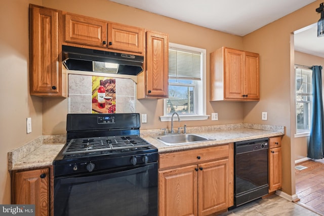 kitchen with light countertops, under cabinet range hood, a sink, a healthy amount of sunlight, and black appliances