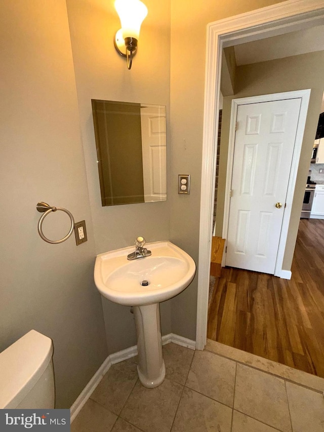 half bathroom featuring baseboards, a sink, tile patterned flooring, and toilet