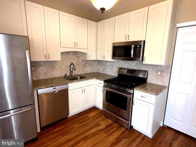 kitchen featuring appliances with stainless steel finishes, a sink, dark wood-style floors, dark stone counters, and white cabinetry