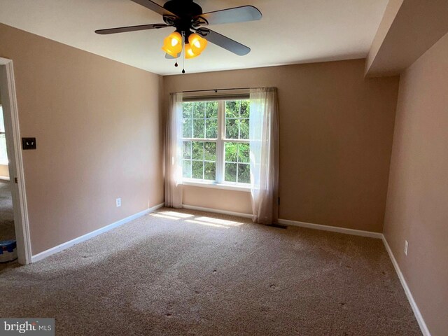 carpeted spare room featuring baseboards and a ceiling fan