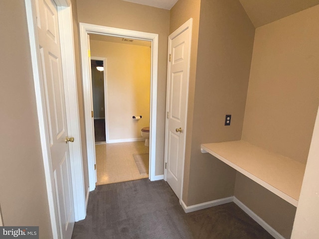 hall featuring baseboards and dark colored carpet