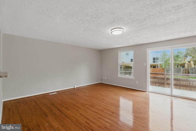 spare room with wood finished floors, a textured ceiling, and baseboards