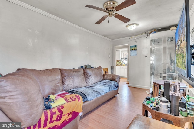 living area featuring baseboards, light wood-style floors, ornamental molding, and a ceiling fan