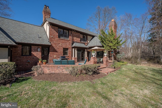 rear view of property with a high end roof, a chimney, a patio area, a yard, and brick siding