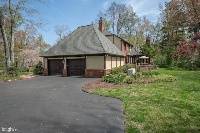 view of side of property with driveway, a chimney, an attached garage, a yard, and brick siding