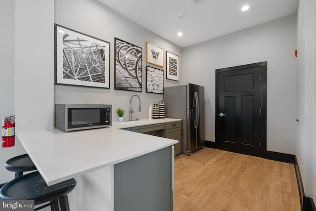 kitchen featuring stainless steel appliances, light wood-type flooring, light countertops, a peninsula, and a breakfast bar