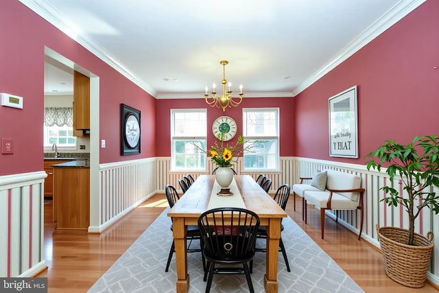 dining area featuring light wood-style floors, crown molding, a notable chandelier, and a wainscoted wall