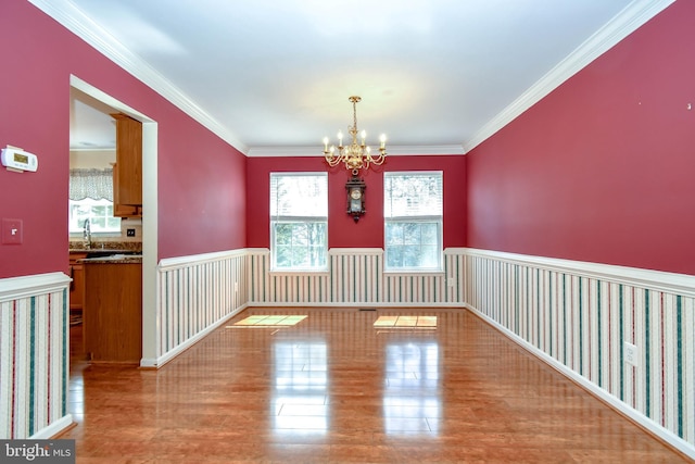 unfurnished dining area with an inviting chandelier, crown molding, and wood finished floors