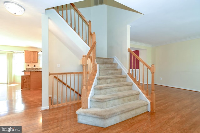 stairway with wood finished floors, visible vents, baseboards, and ornamental molding