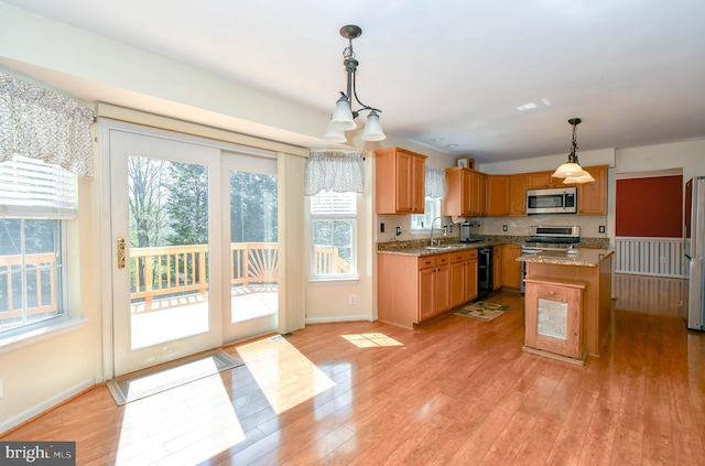 kitchen with light wood-type flooring, stainless steel appliances, a center island, and decorative light fixtures