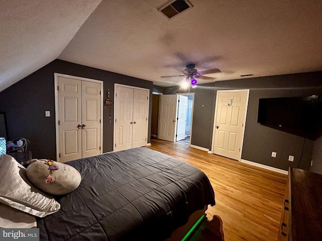 bedroom with wood finished floors, a textured ceiling, two closets, baseboards, and visible vents