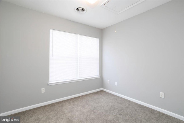 carpeted spare room with baseboards, visible vents, and attic access