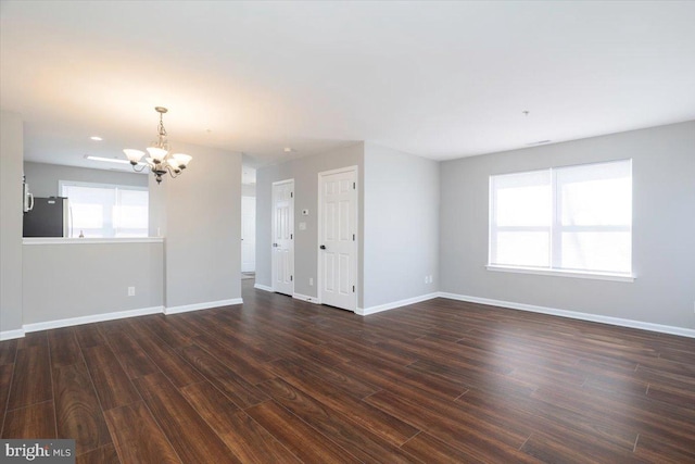 unfurnished living room featuring baseboards, dark wood-style floors, and a notable chandelier