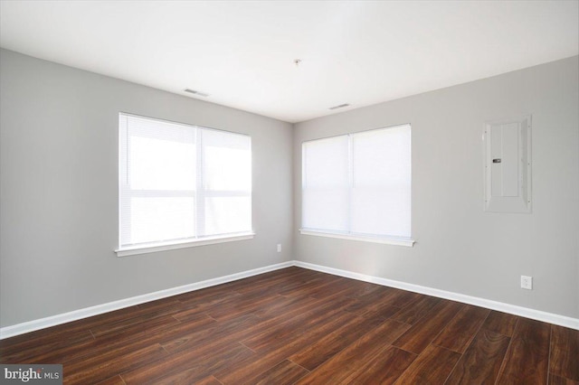 spare room featuring baseboards, dark wood-style flooring, visible vents, and electric panel