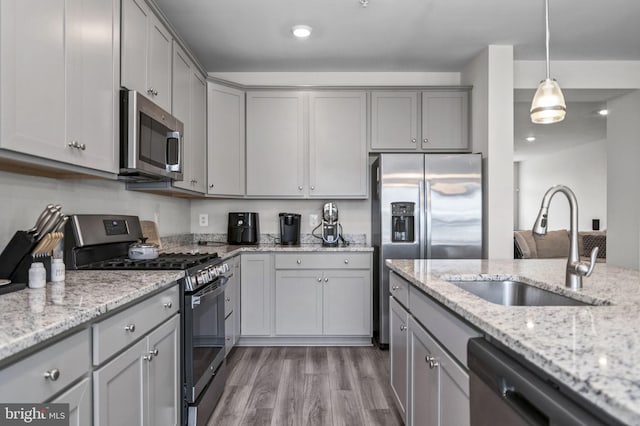 kitchen with light wood finished floors, stainless steel appliances, gray cabinetry, and a sink